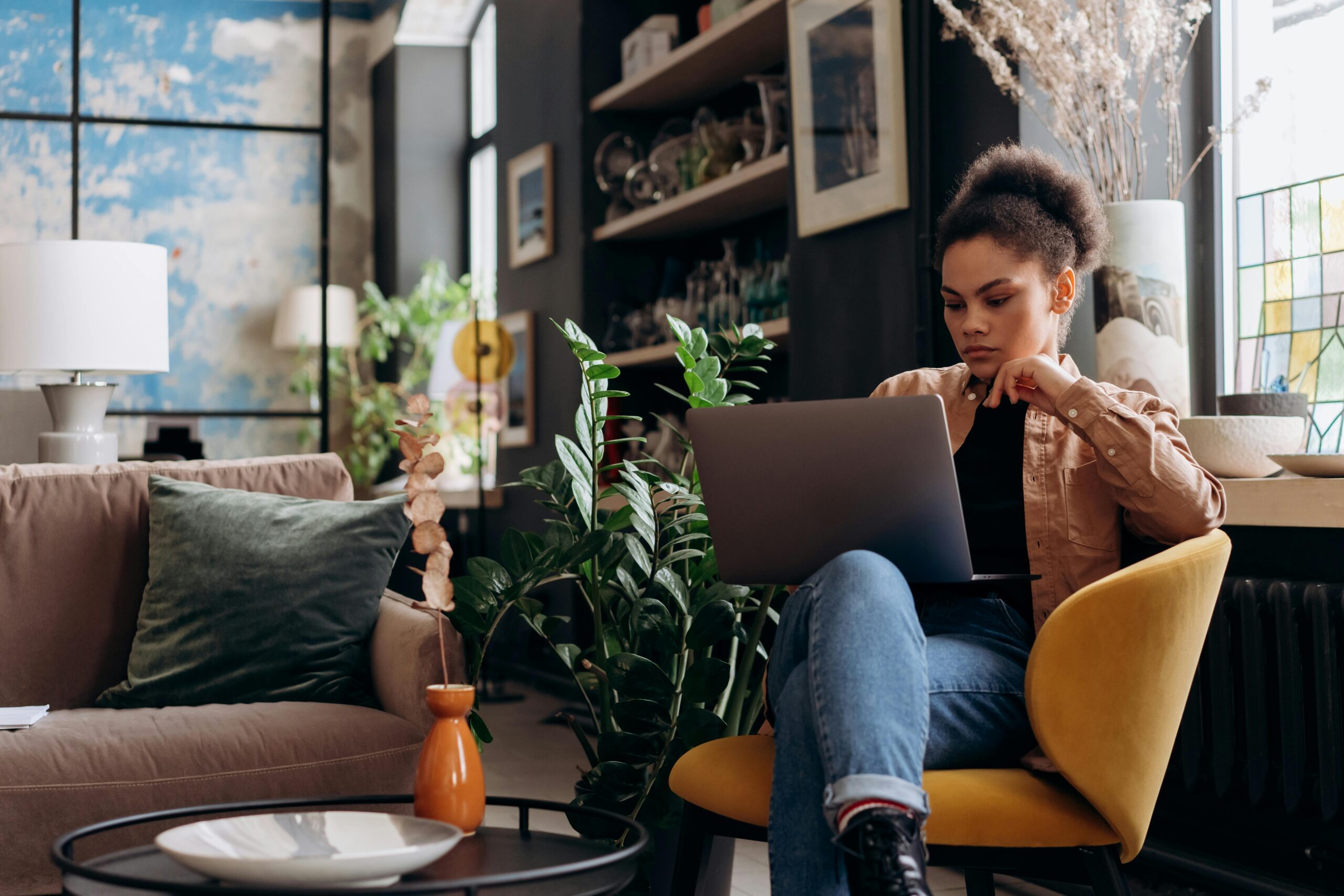 Focused woman working on laptop in a stylish home office environment, emphasizing a modern and relaxed work setting.